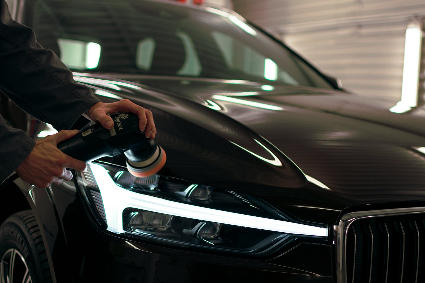 Hands polishing a black car hood with a buffer.