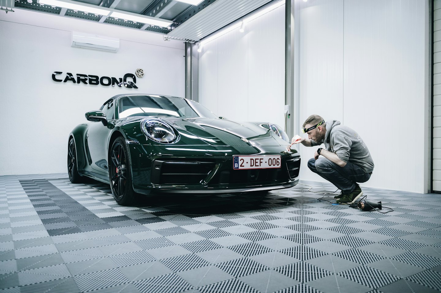 Man detailing luxury sports car bumper in modern garage.