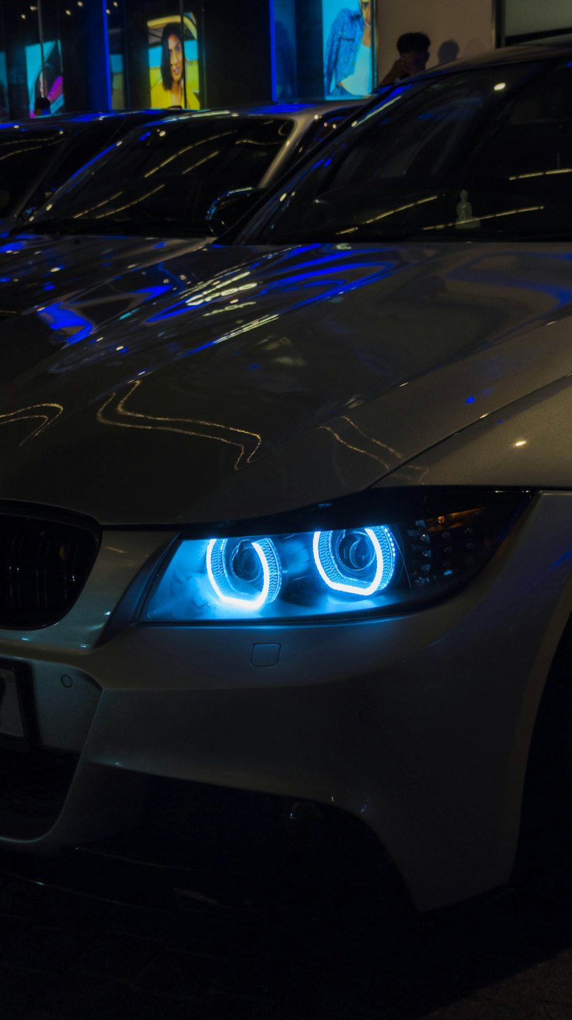 A silver car with glowing blue LED headlights at night.