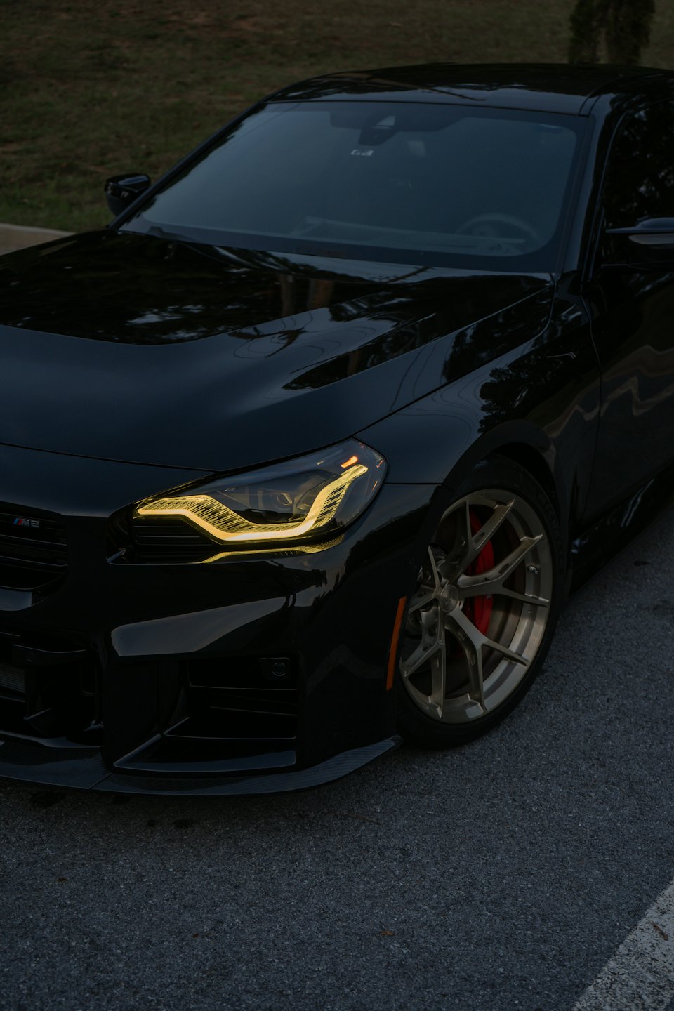 Sleek black sports car with glowing headlights and gold wheels parked at night.