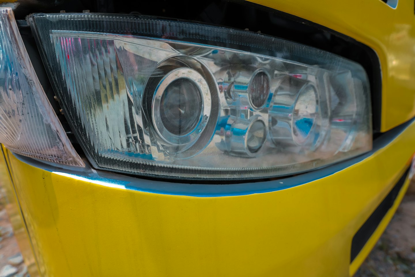 Clear car headlight with complex lenses on a yellow car.