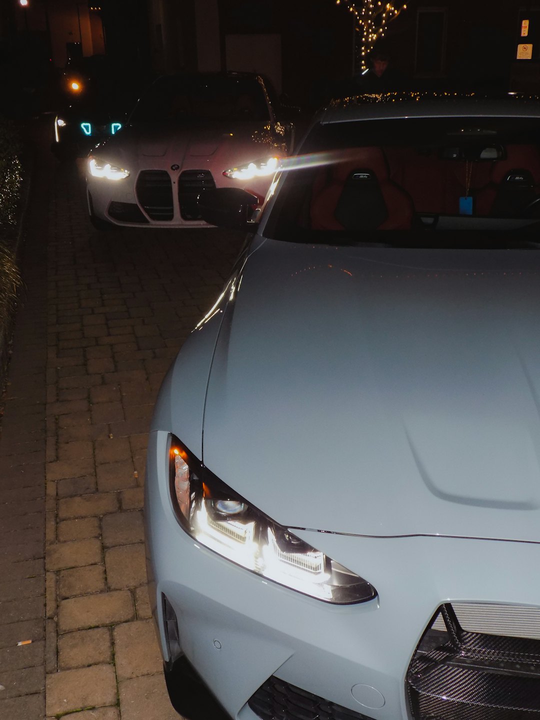 Two luxury cars parked on a driveway at night, headlights on.