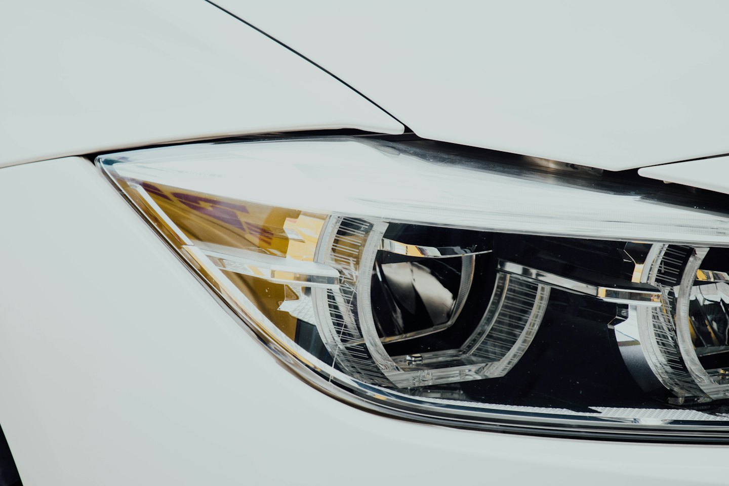 The clear headlight lens and internal reflectors of a white car.