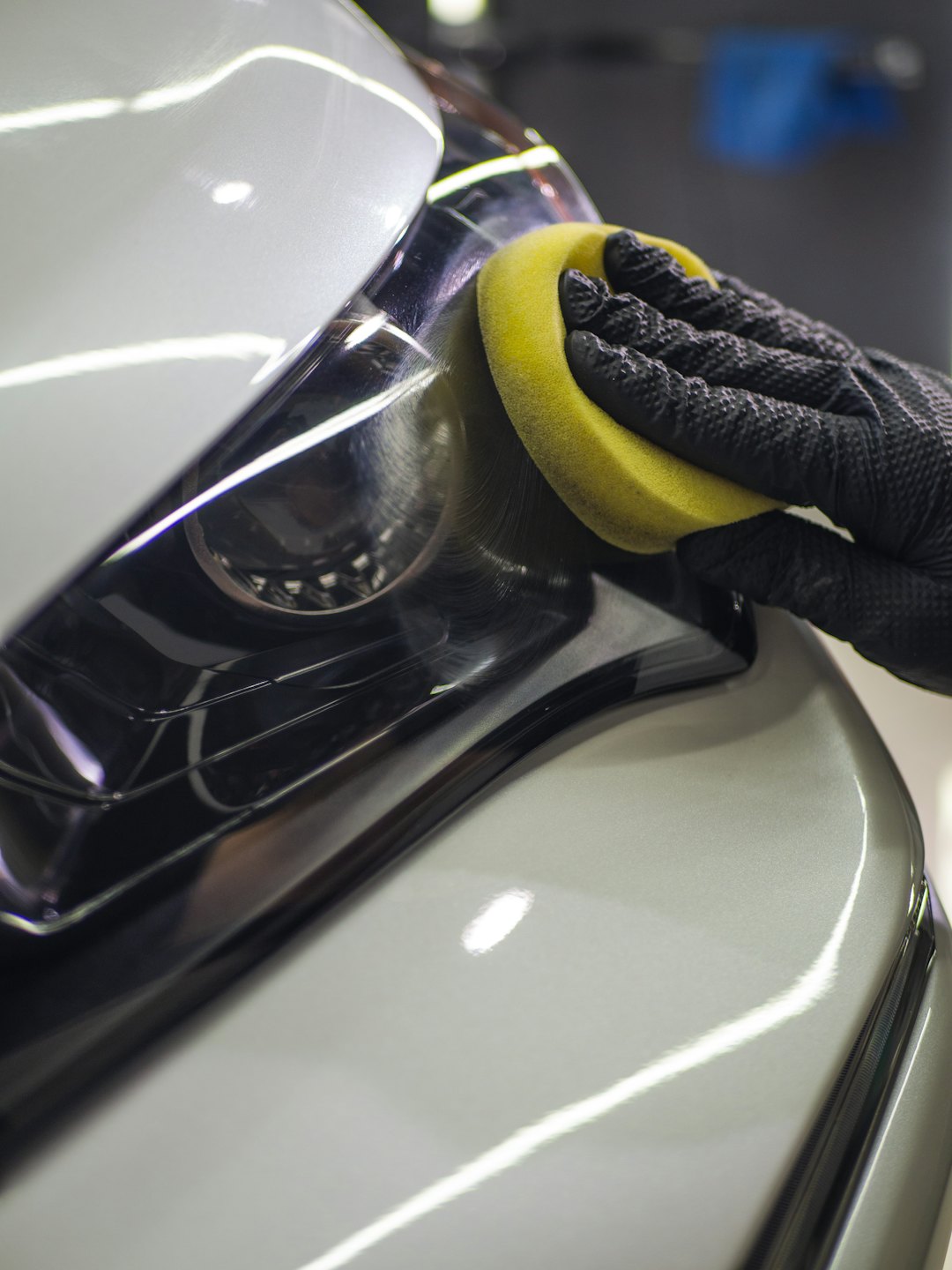 A person polishes a car headlight with a yellow sponge.