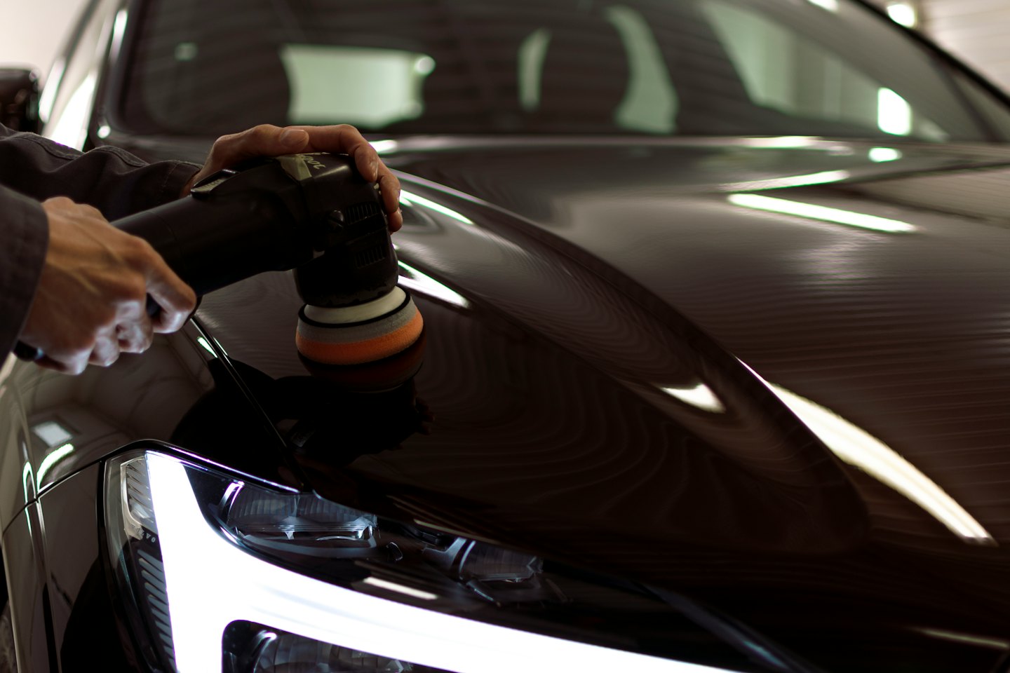 Hands buffing a car hood with a polisher.
